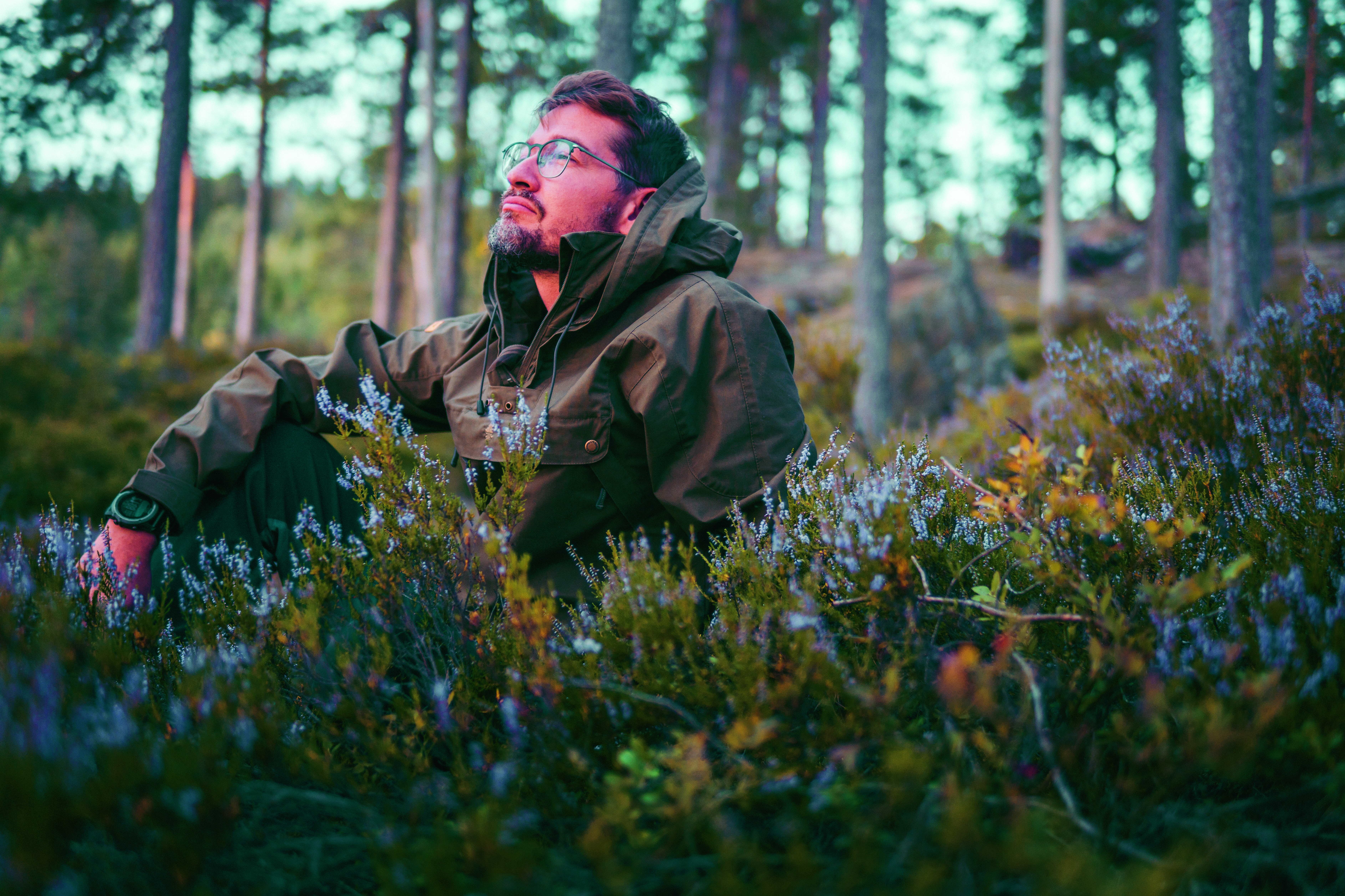 Man zit in het bos tussen de bloemen, kijkt weg